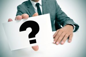 a man wearing a suit sitting in a desk holding a signboard with a question mark